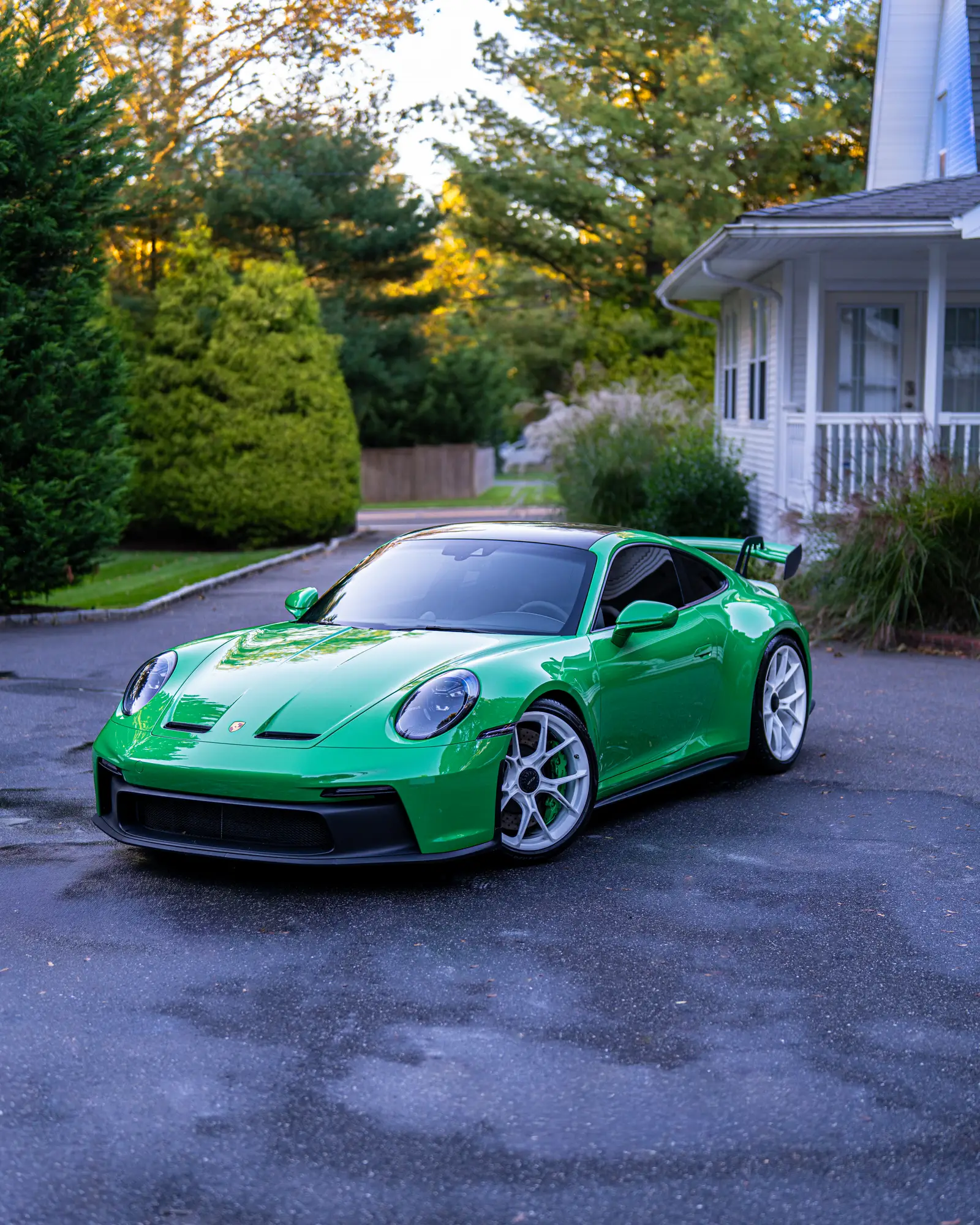 Green Porsche 911 GT3 parked outside a shingled house at dusk